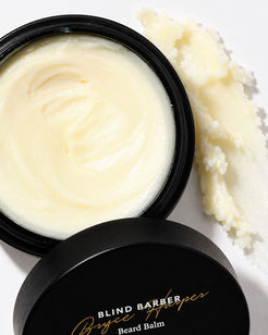 An open black jar of Blind Barber Bryce Harper Beard Balm with creamy off-white balm visible, alongside a smear of the balm on a white background.