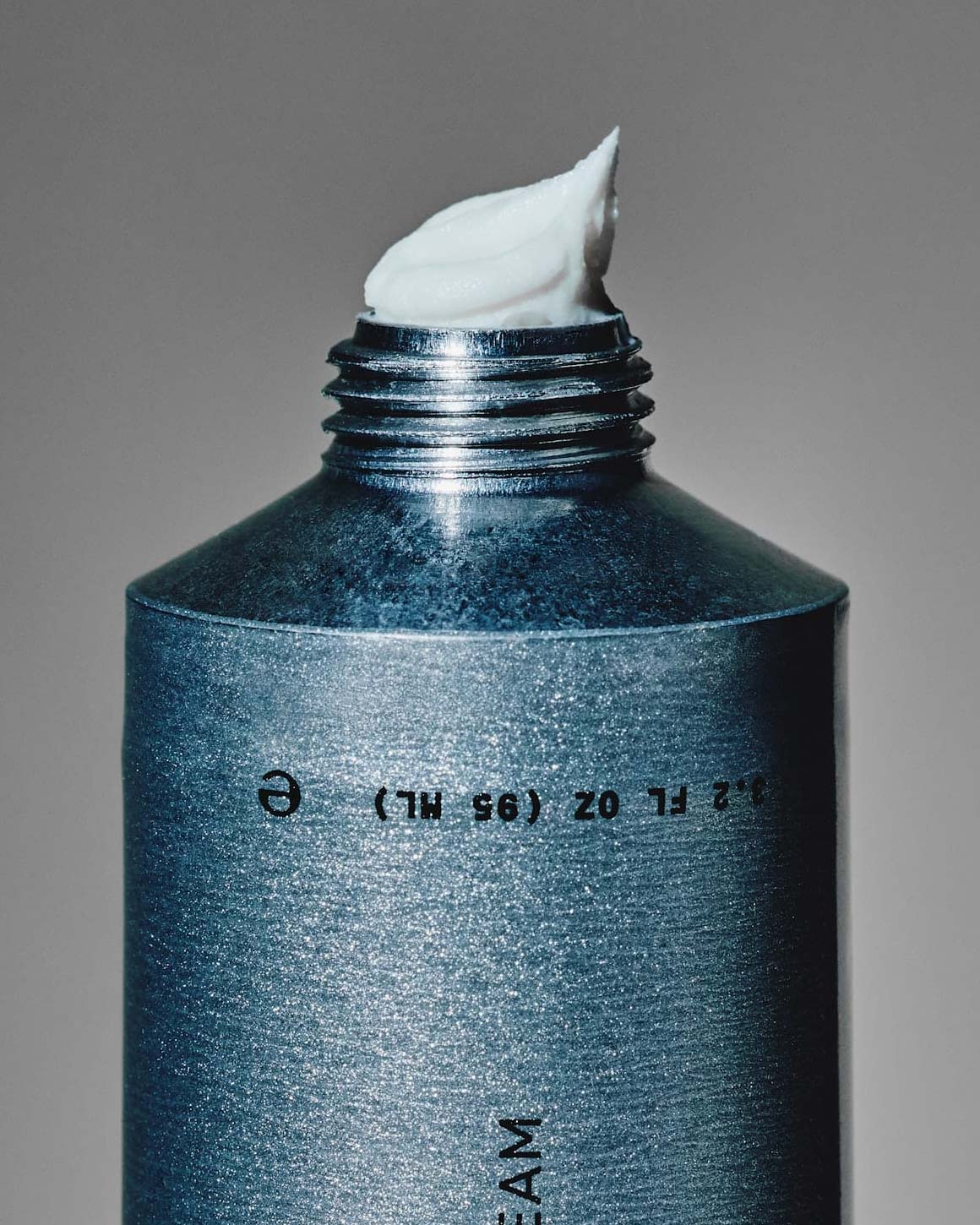 Close-up of white Firsthand Supply Effortless Air Crème styling cream at the opening of an uncapped silver tube.