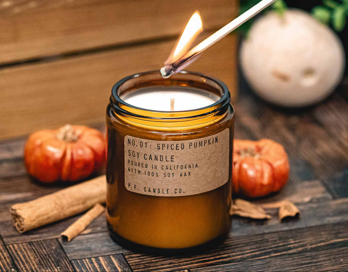An amber glass jar candle with a kraft paper label reading 'No. 0F: Spiced Pumpkin' and 'Puffed in California by San Diego Soy Wax Co.
