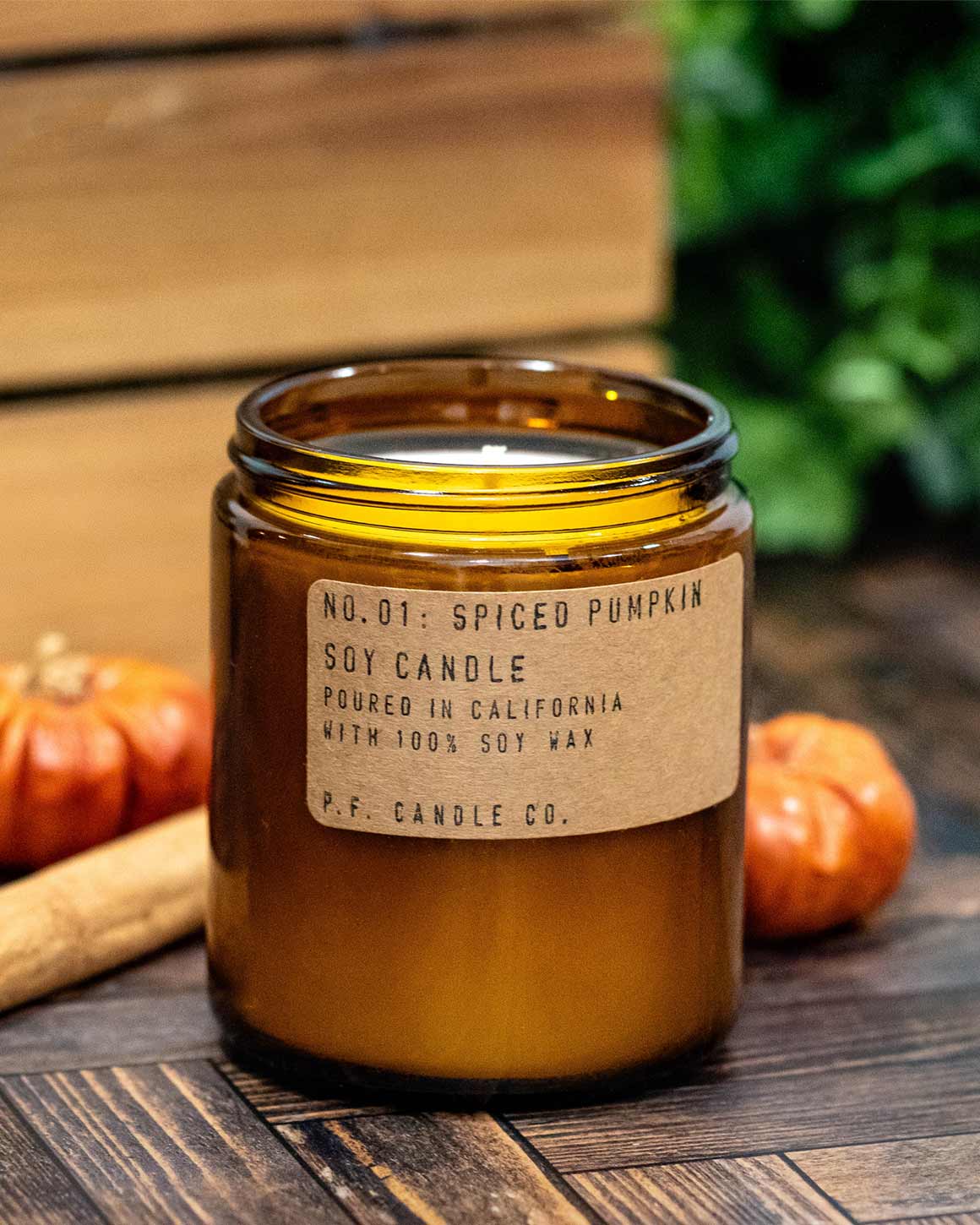 Spiced pumpkin soy candle with a label on a wooden surface with pumpkins and cinnamon sticks.