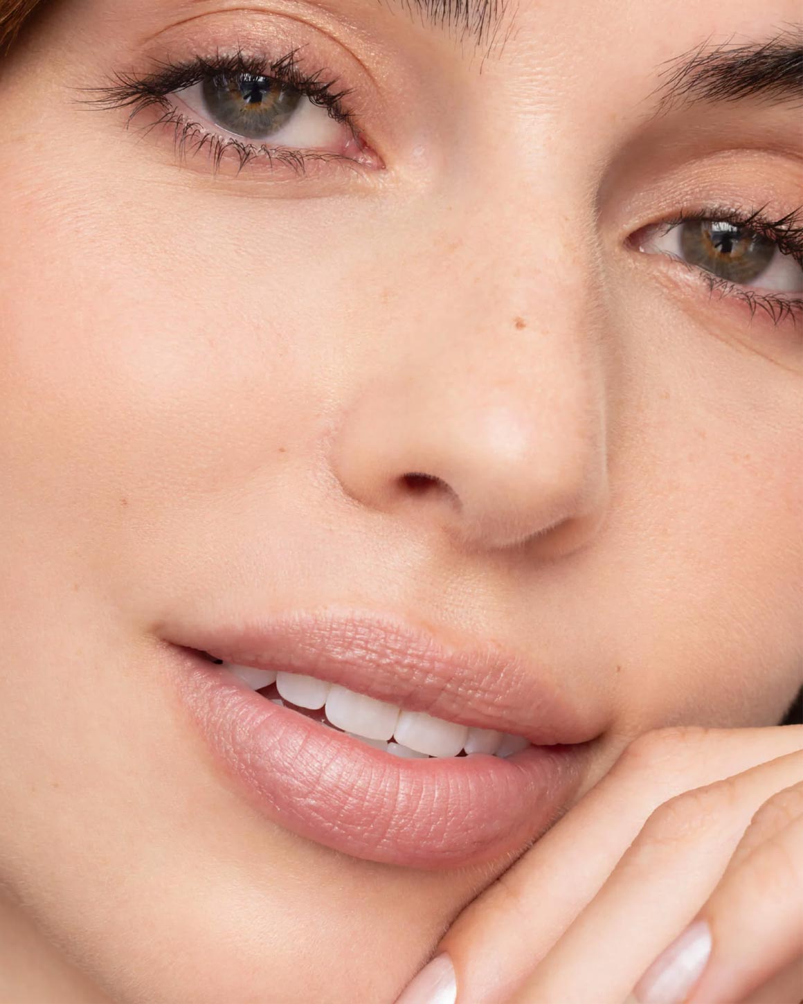 Close-up of a woman's face showing natural, matte pink lipstick on her lips, with clear skin and subtle freckles.